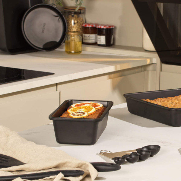 Black non-stick loaf tin with baked loaf topped with dried citrus slices, kitchen setting