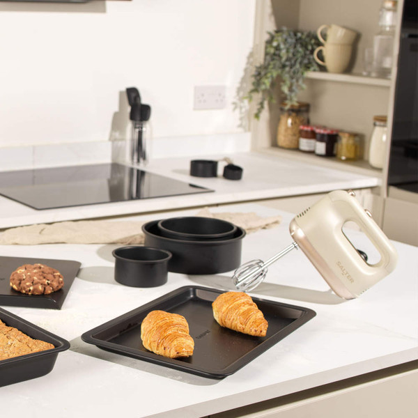 Baking tray and tins with croissants, cookie and hand mixer on kitchen counter