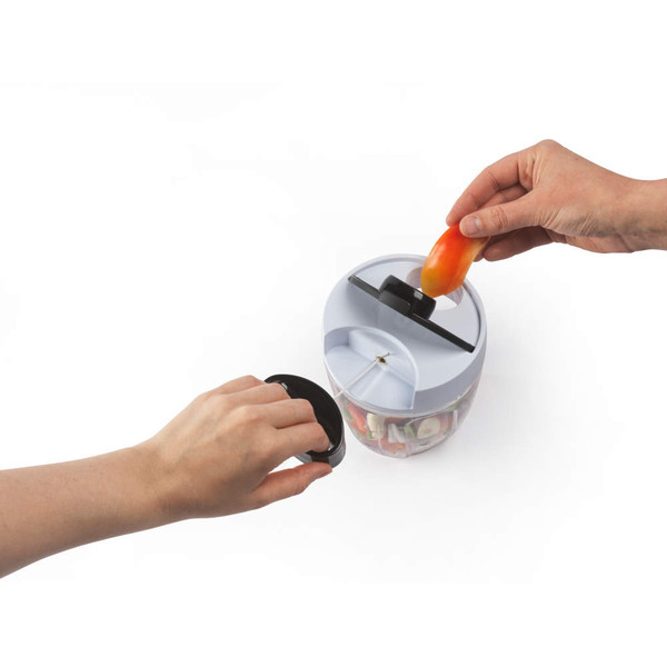 Manual food chopper with hands adding tomato, for dicing vegetables at home.
