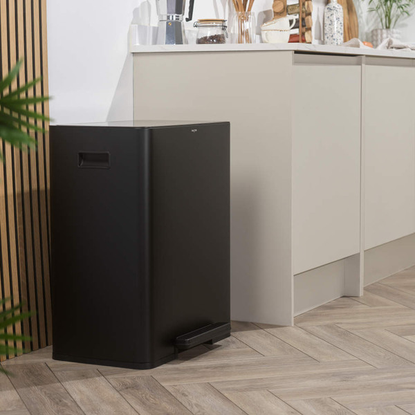 Black rectangular kitchen pedal bin with flat lid next to beige cupboards