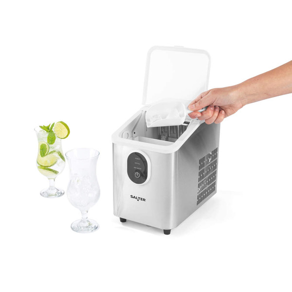 Hand scooping ice from silver home ice maker, with two glasses, one with mojito cocktail and lime.