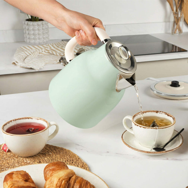 Light green stovetop kettle pouring hot water into teacup in kitchen setting