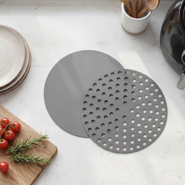 Set of two round grey air fryer liners, one solid and one with holes, on kitchen worktop
