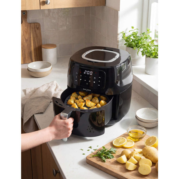 Black digital air fryer cooking seasoned potato chunks on kitchen counter