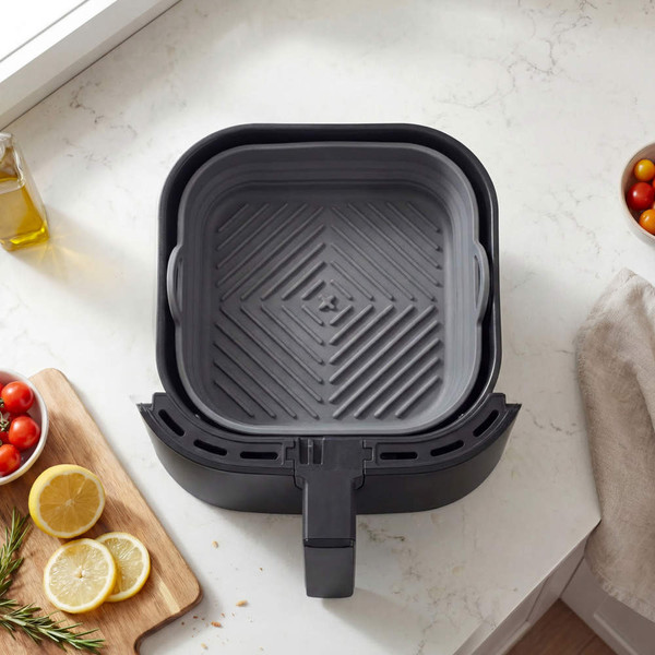 Grey silicone air fryer liner in square shape, placed inside black air fryer basket