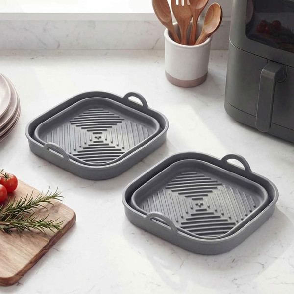 Set of two grey silicone air fryer liners with handles on kitchen worktop