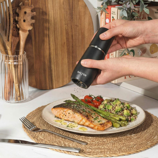 Black electric salt or pepper grinder seasoning salmon fillet and vegetables on plate