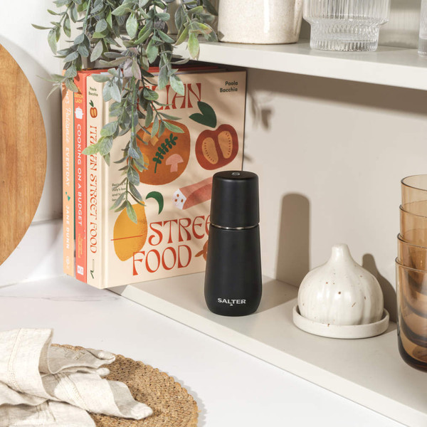 Black electric grinder seasoning chicken and salad on plate, kitchen counter setting