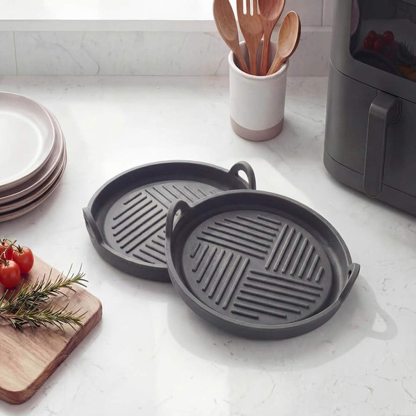 Two round black grill pans with handles on a kitchen counter
