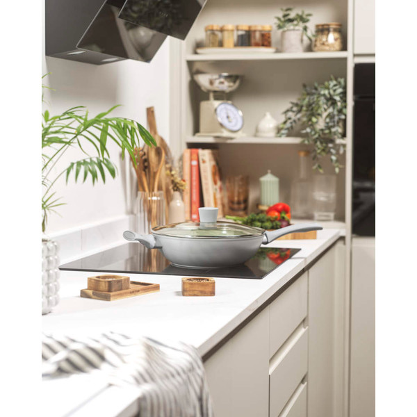 Green non-stick frying pan with glass lid on modern kitchen hob