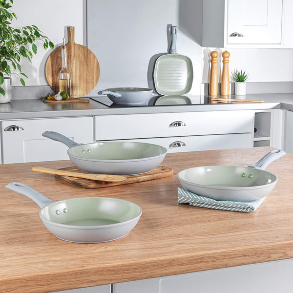 Set of three grey non-stick frying pans with green interior on kitchen worktop