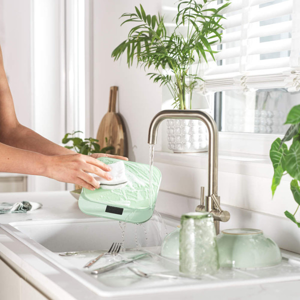 Person washing light green food container under tap in bright kitchen sink