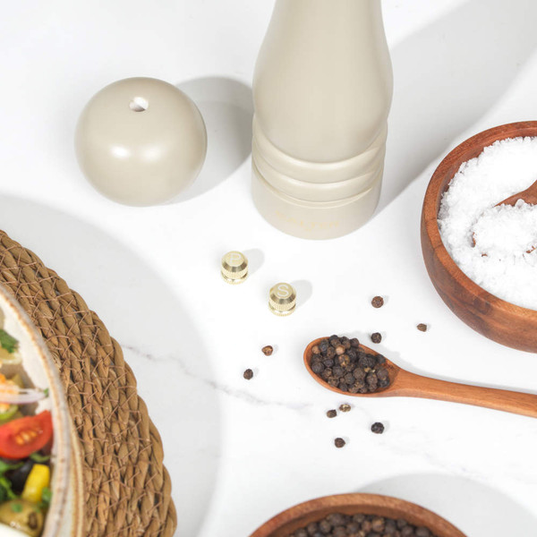 Beige salt and pepper mills with wooden bowls of salt and pepper on white worktop