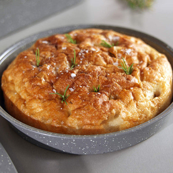 Freshly baked focaccia bread topped with sea salt and rosemary in round tin