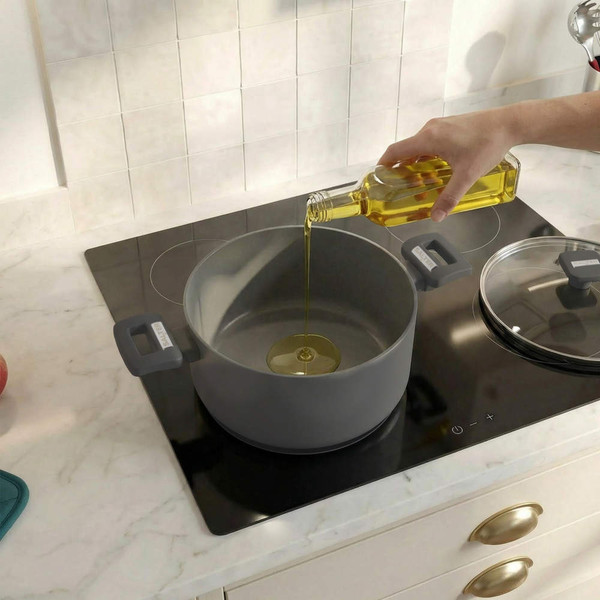 Grey non-stick casserole pot on hob with oil being poured in