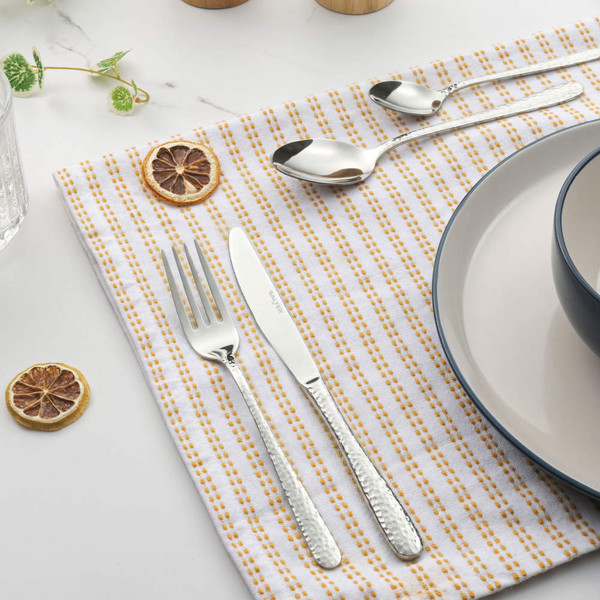 Set of silver hammered cutlery on striped napkin beside plate and dried citrus slice