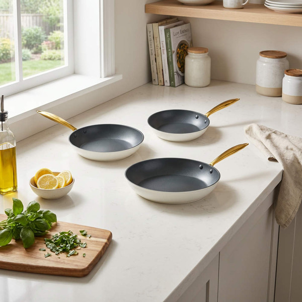 Set of three non-stick frying pans with gold handles on a kitchen countertop