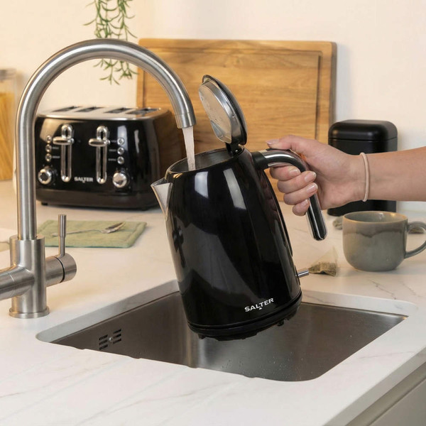 Black electric kettle being filled at kitchen sink, shown from side with lid open