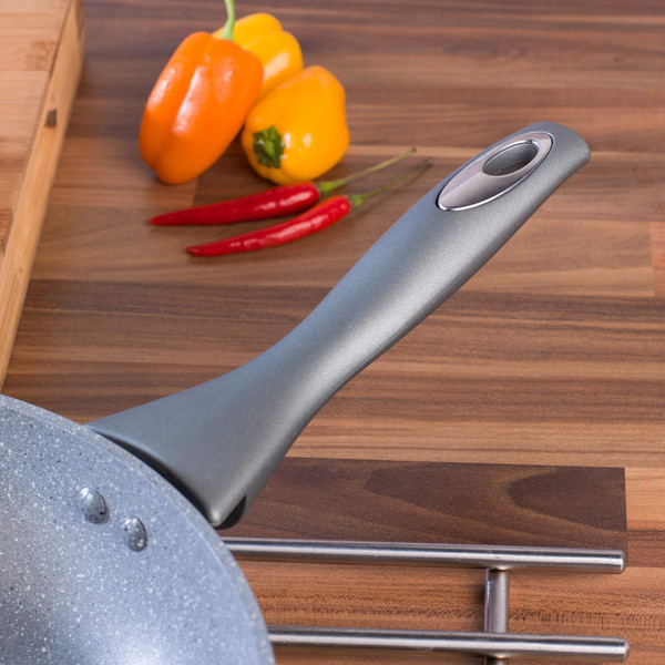 Grey non-stick frying pan handle close-up on wood worktop with peppers and chillies.