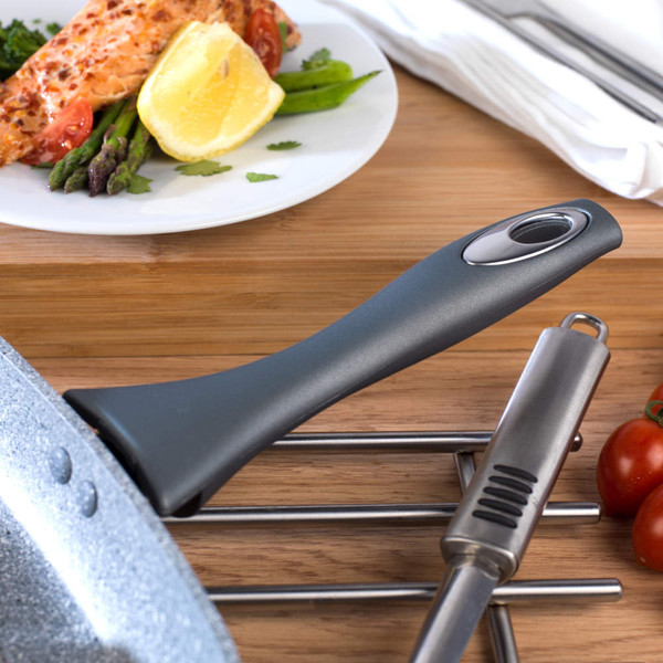 Grey non-stick frying pan handle close-up on wooden worktop beside kitchen utensils