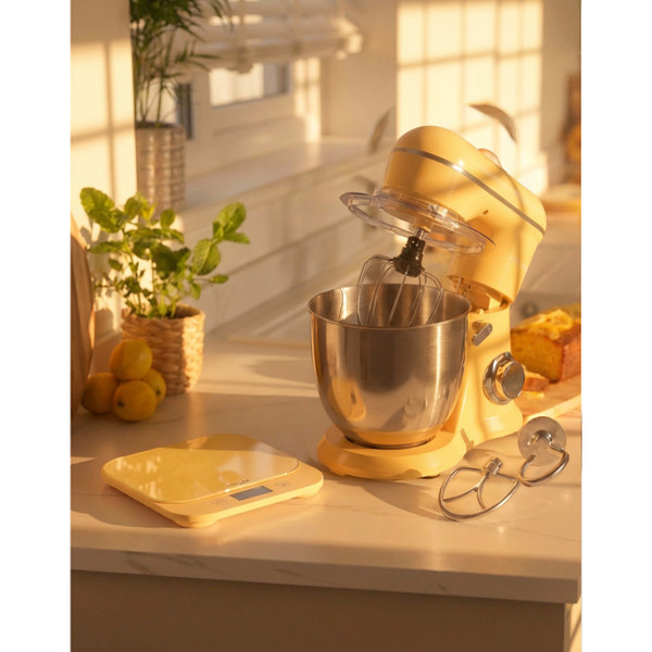 Yellow stand mixer with stainless steel bowl and attachments on kitchen counter in sunlight