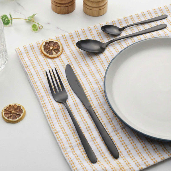 Matte black cutlery set with fork, knife, and spoons beside plate on patterned napkin