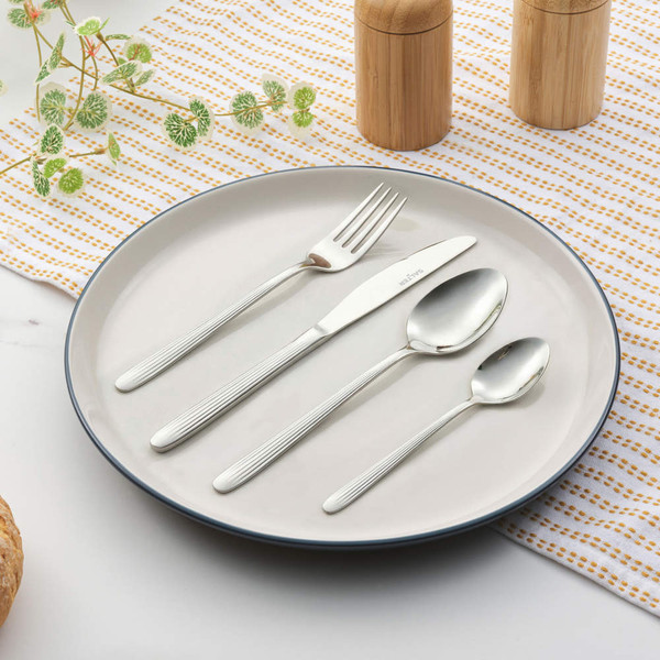 Set of four silver striped cutlery pieces on plate, including fork, knife, spoon and teaspoon.