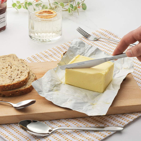 Stainless steel butter knife spreading butter on a wooden board with seeded bread slices