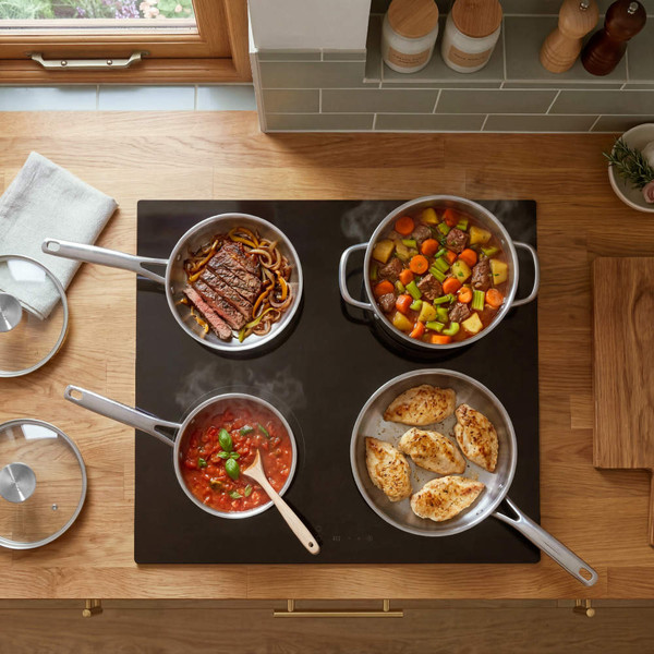 Silver pans cooking steak, chicken, stew and tomato sauce on electric hob, kitchen setting