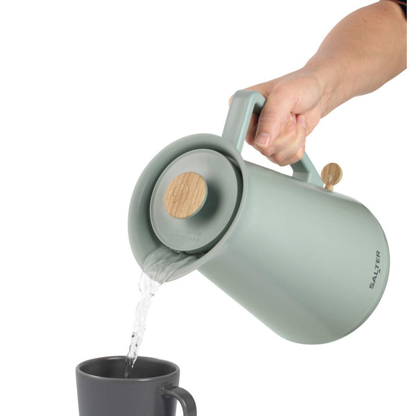Sage green electric kettle pouring hot water into a grey mug, shown in use.