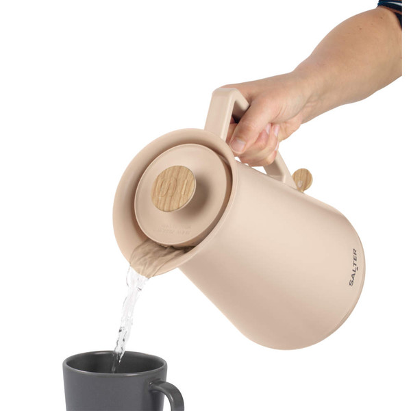 Beige electric kettle with wood accents pouring hot water into black mug