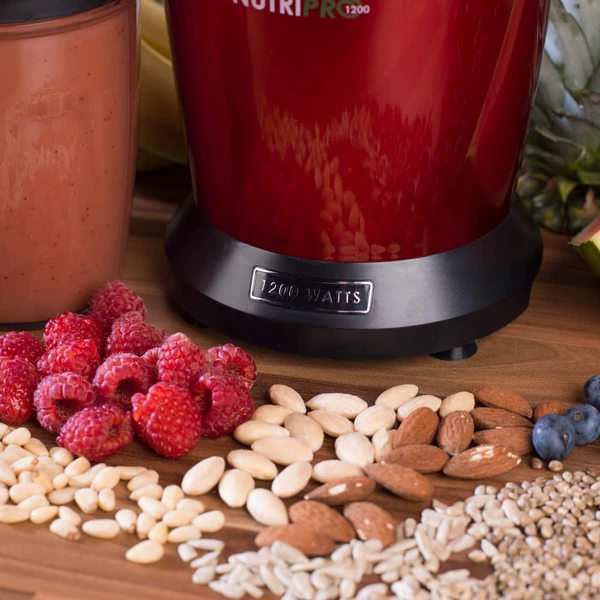 Red blender base and smoothie with berries and nuts, countertop product image.
