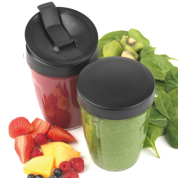 Two blender cups with black lids, one with red smoothie, one with green smoothie, fresh fruit beside.