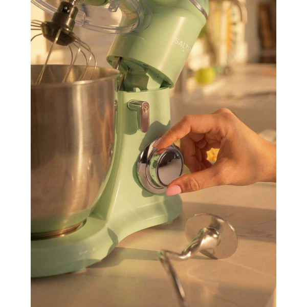 Green stand mixer with large metal bowl, person adjusting speed dial, dough hook on counter