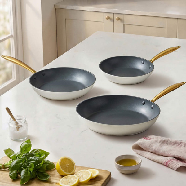 Set of three non-stick frying pans with gold handles on kitchen countertop