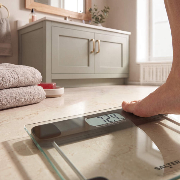 Black glass bathroom scale with digital display showing weight, foot stepping on scale