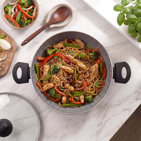 Stir fry with chicken, noodles, broccoli and peppers in a non-stick wok on a kitchen counter