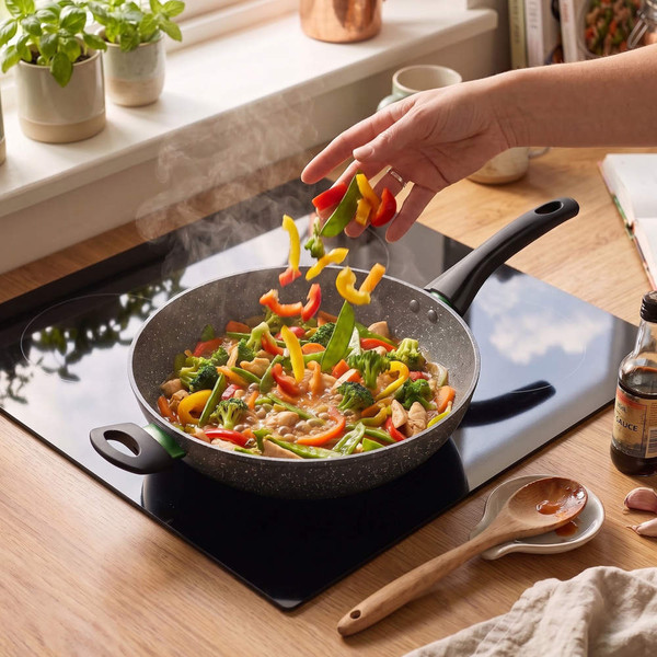 Cooking stir-fry with colourful vegetables in a non-stick frying pan on hob