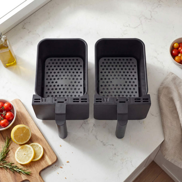 Dual black air fryer baskets on kitchen counter, shown empty from above