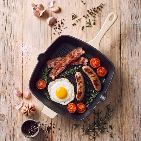 Square cream grill pan with cooked bacon, sausages, egg and tomatoes on wooden surface