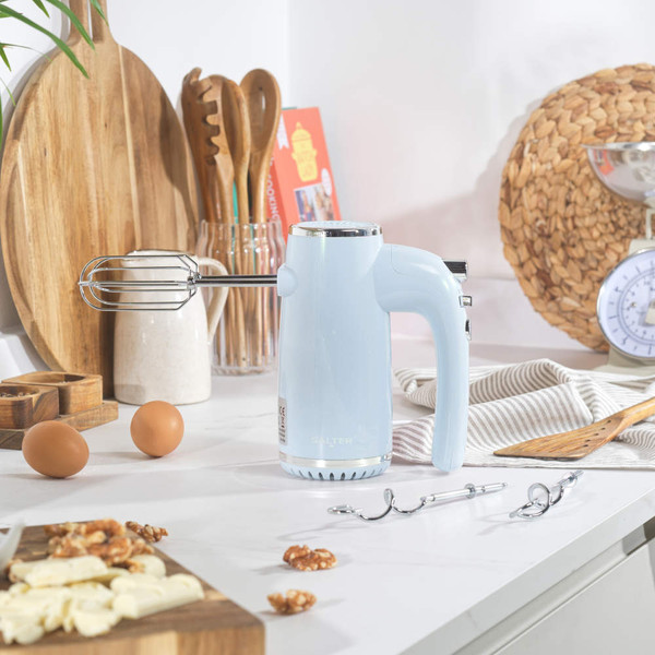 Light blue electric hand mixer on kitchen counter with attachments and baking ingredients