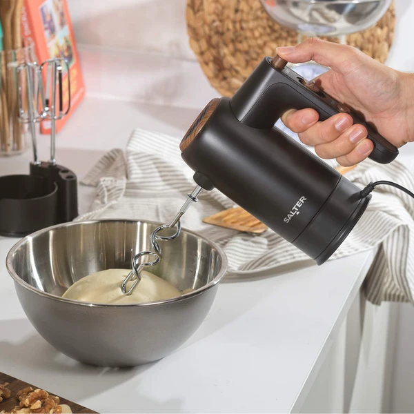 Black electric hand mixer with dough hook mixing dough in a silver bowl on kitchen worktop