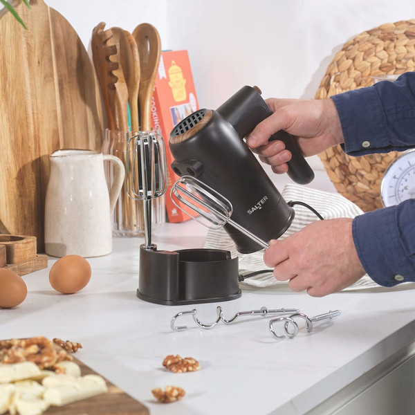 Black hand mixer with chrome beaters and accessories on kitchen counter
