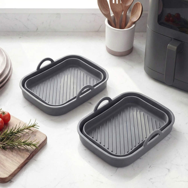 Set of two grey silicone air fryer trays with handles, shown on kitchen worktop.