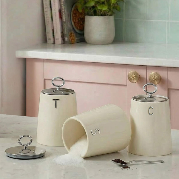 Cream kitchen storage jars for tea, sugar and coffee, shown on countertop.