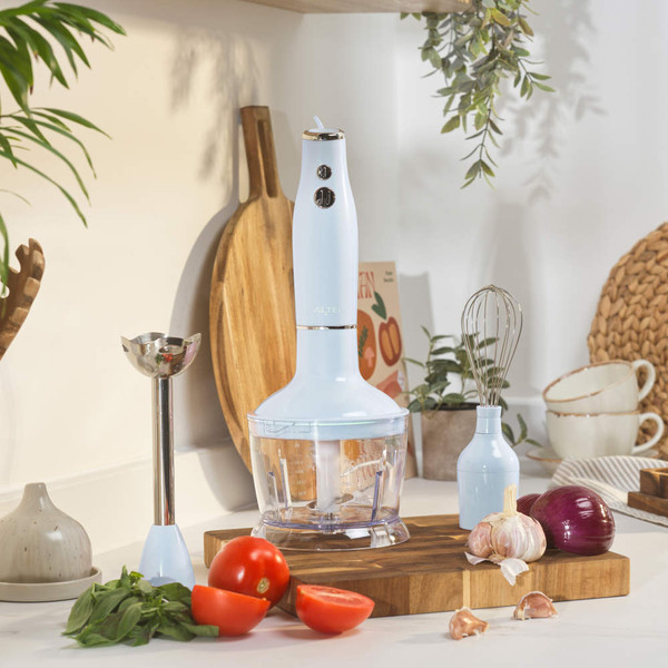 Light blue hand blender set with attachments on kitchen counter, surrounded by fresh vegetables