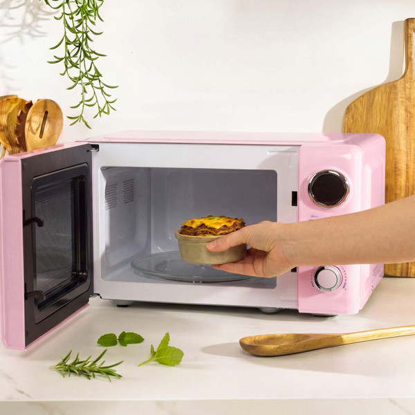Pink microwave with open door, hand removing small pie on kitchen counter