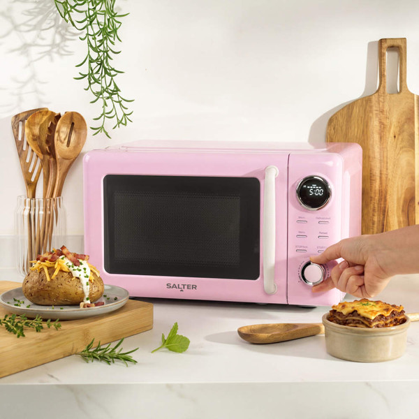 Pink microwave oven with digital display, shown on a kitchen counter with cooked food