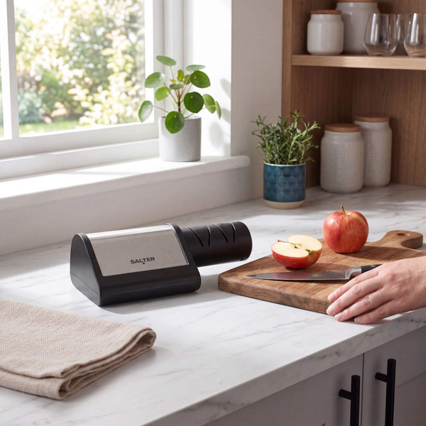 Electric knife sharpener on kitchen counter beside apples and chopping board