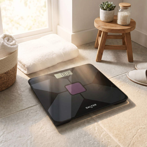 Black digital bathroom scale with display, on tiled floor in sunlight